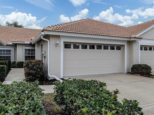 view of side of home featuring stucco siding, driveway, an attached garage, and a tile roof