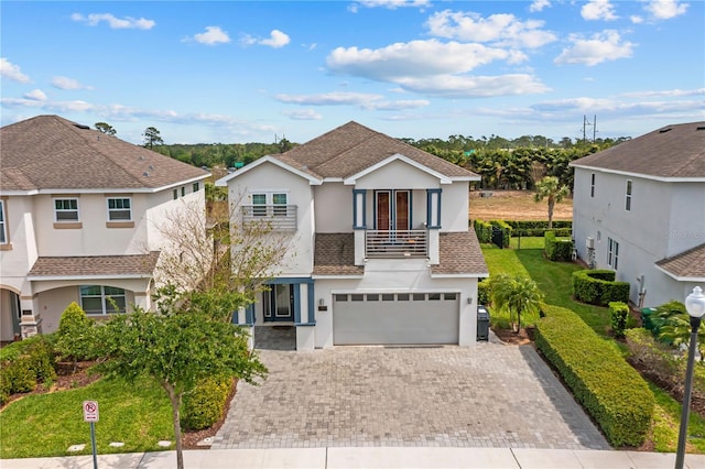 view of front of home featuring a front lawn, stucco siding, driveway, a balcony, and an attached garage