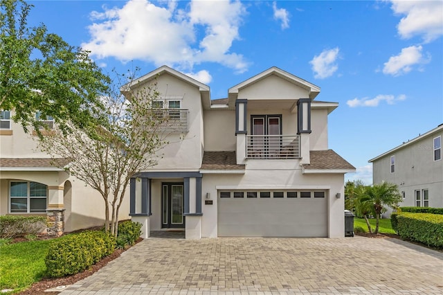 view of front of house with a balcony, stucco siding, decorative driveway, and a garage