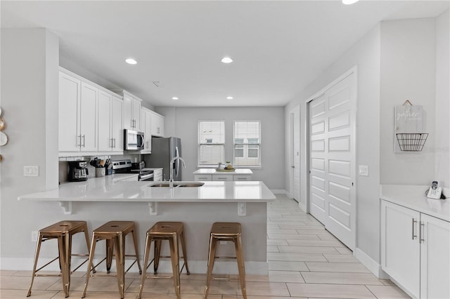 kitchen with a kitchen bar, a sink, stainless steel appliances, a peninsula, and white cabinets