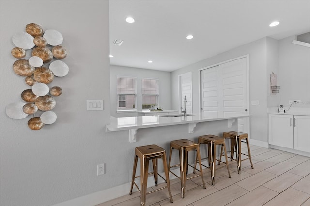 kitchen with visible vents, a breakfast bar area, light countertops, white cabinetry, and a sink