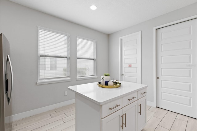 kitchen featuring baseboards, stainless steel fridge, light countertops, and white cabinetry