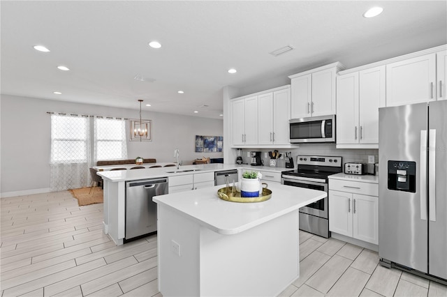 kitchen with a sink, a kitchen island, stainless steel appliances, a peninsula, and light countertops