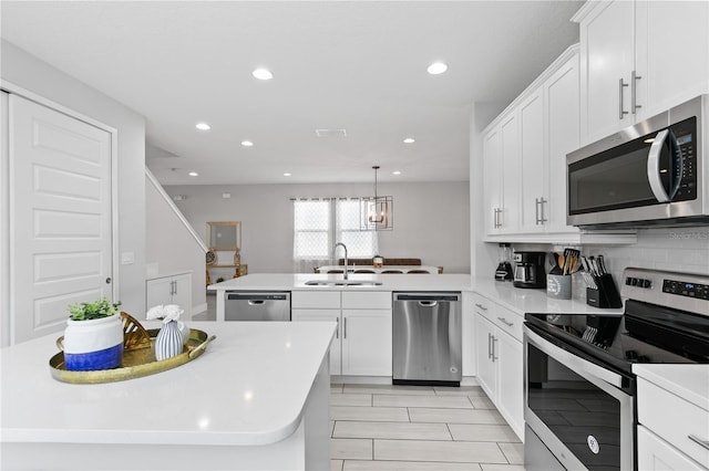 kitchen with a peninsula, a sink, light countertops, appliances with stainless steel finishes, and white cabinetry