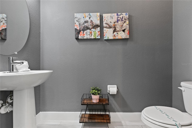 bathroom with toilet, a textured wall, baseboards, and a sink