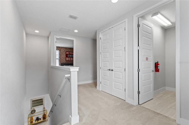 corridor with an upstairs landing, visible vents, light colored carpet, and baseboards