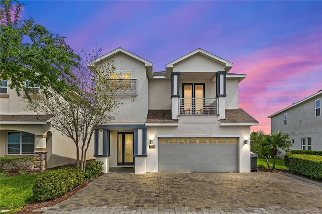 view of front of house featuring stucco siding, an attached garage, decorative driveway, and a balcony