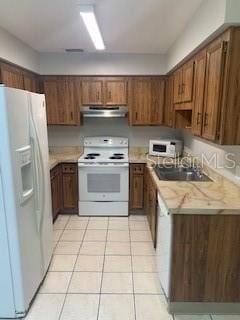 kitchen with under cabinet range hood, light countertops, light tile patterned floors, white appliances, and a sink