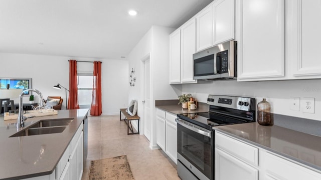 kitchen featuring light tile patterned floors, a sink, white cabinets, appliances with stainless steel finishes, and dark countertops