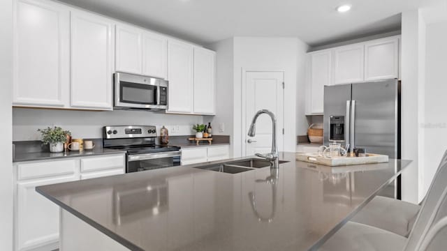 kitchen with dark countertops, an island with sink, appliances with stainless steel finishes, white cabinets, and a sink