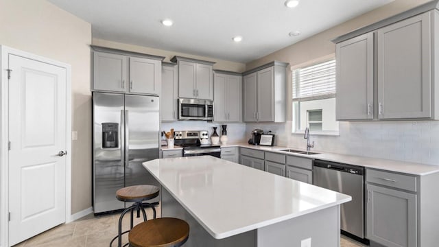 kitchen featuring a breakfast bar area, gray cabinets, a sink, appliances with stainless steel finishes, and a center island