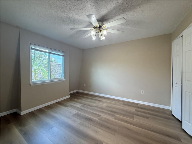 unfurnished bedroom with ceiling fan, wood finished floors, baseboards, and a textured ceiling