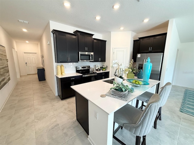945 Laurel View Way, Groveland, FL 34736 - kitchen featuring appliances with stainless steel finishes, dark cabinets, a center island with sink, a kitchen bar, and light countertops