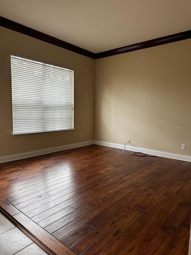 empty room with dark wood finished floors, baseboards, and ornamental molding