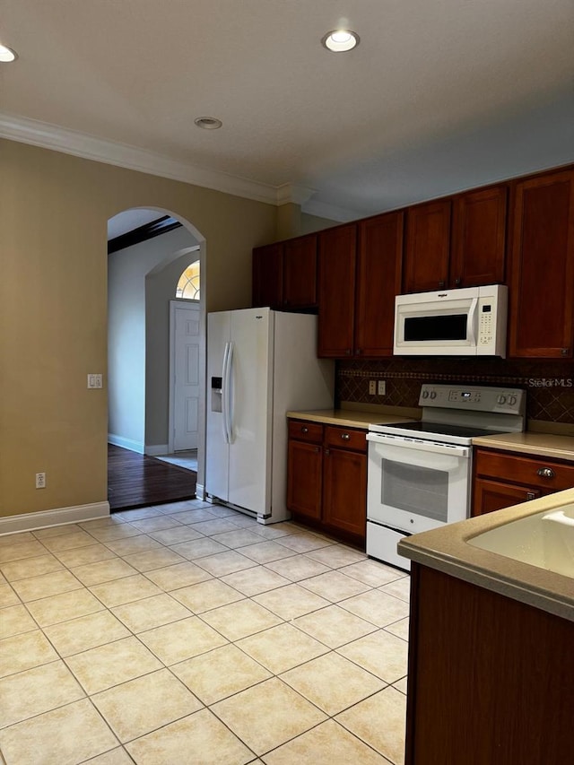 kitchen with light tile patterned floors, white appliances, arched walkways, and ornamental molding