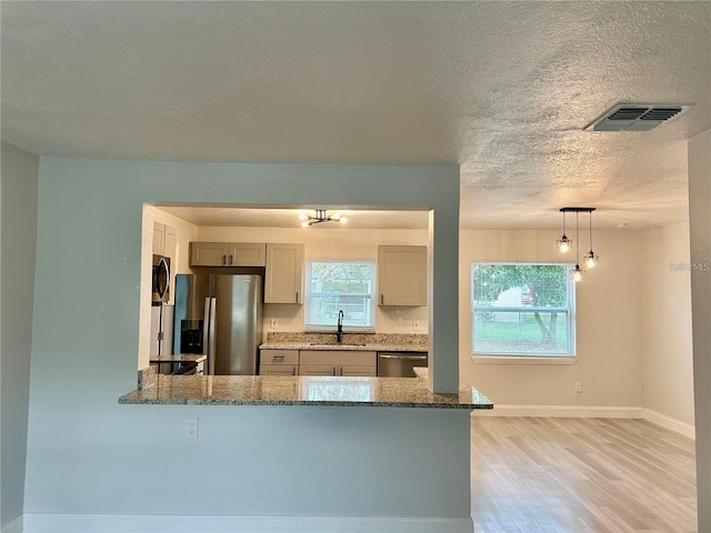 kitchen with stone counters, light wood finished floors, a peninsula, a sink, and appliances with stainless steel finishes