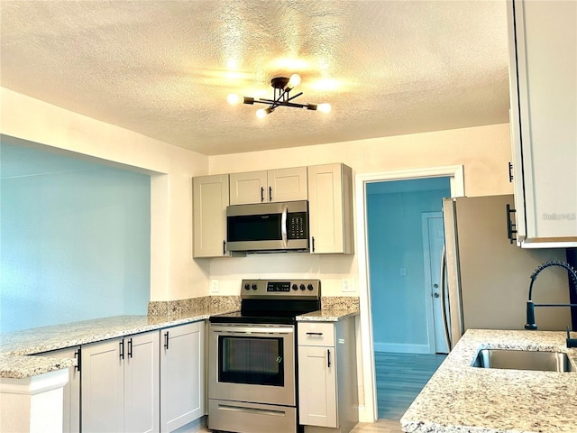 kitchen featuring a sink, light wood-style floors, appliances with stainless steel finishes, a peninsula, and light stone countertops