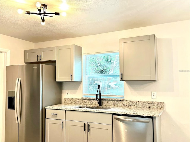 kitchen with light stone counters, gray cabinets, stainless steel appliances, a textured ceiling, and a sink