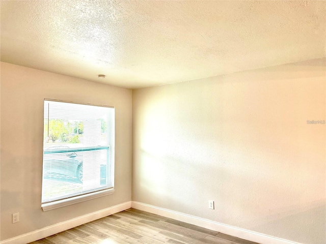 unfurnished room with baseboards, light wood-type flooring, and a textured ceiling