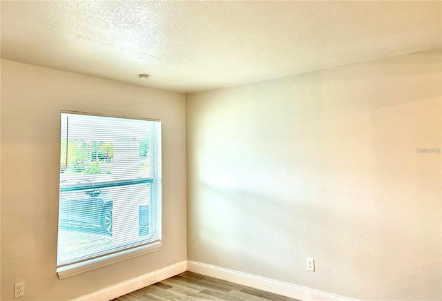 empty room featuring a textured ceiling, baseboards, and light wood-style floors