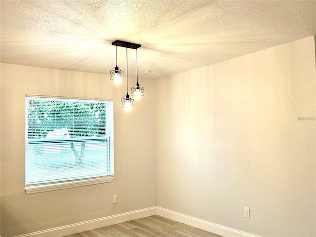 empty room featuring baseboards, light wood finished floors, and a textured ceiling