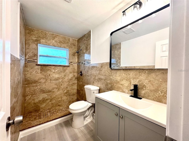 full bathroom featuring tile walls, toilet, a tile shower, wood finished floors, and vanity