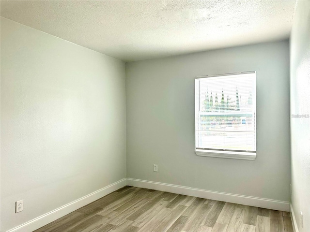 empty room featuring baseboards, light wood-type flooring, and a textured ceiling