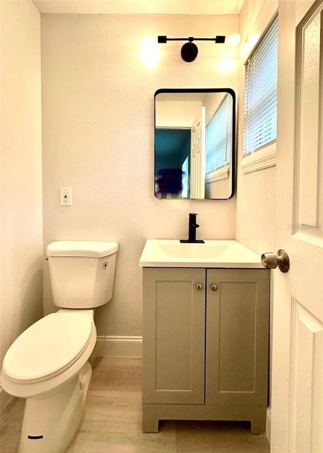 half bathroom with baseboards, toilet, wood finished floors, and vanity