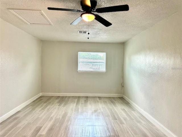 unfurnished room featuring visible vents, baseboards, light wood-style floors, and a textured wall