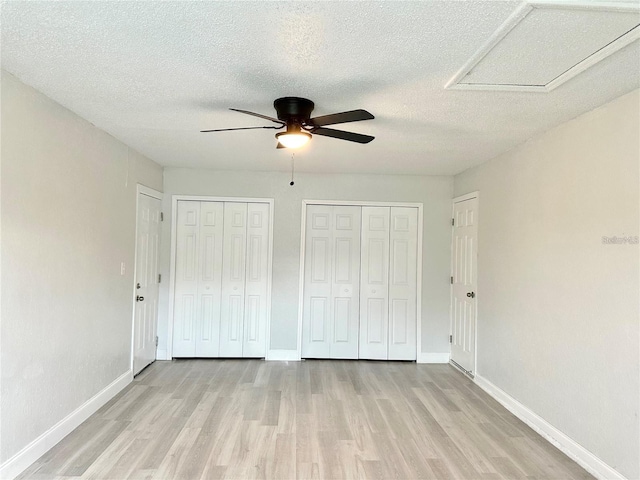 unfurnished bedroom with a ceiling fan, baseboards, light wood-style floors, a textured ceiling, and two closets