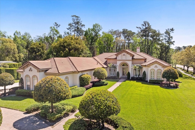 mediterranean / spanish house featuring stucco siding, a chimney, a front yard, and a tile roof