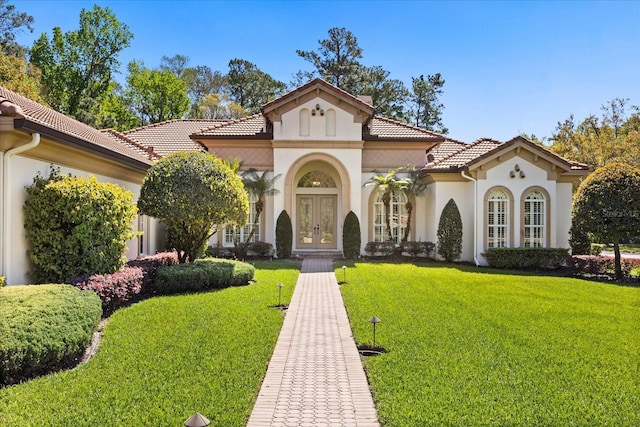 mediterranean / spanish-style house with french doors, stucco siding, a front yard, and a tile roof