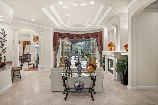 living area featuring a raised ceiling, arched walkways, crown molding, baseboards, and ornate columns