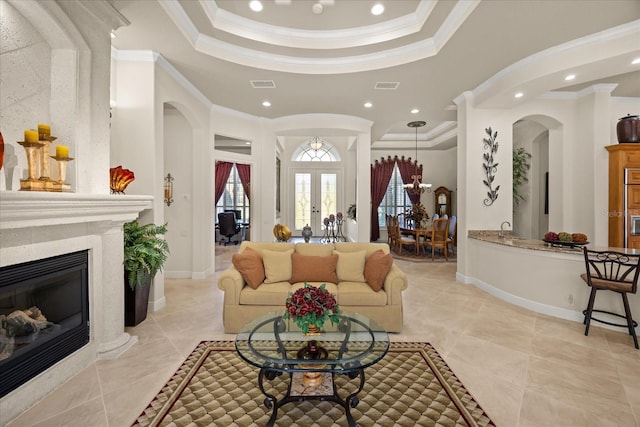 living area with a tray ceiling, visible vents, arched walkways, and ornamental molding