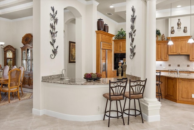 kitchen with tasteful backsplash, a breakfast bar area, ornamental molding, light stone counters, and arched walkways