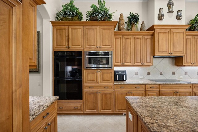 kitchen featuring brown cabinets, black appliances, backsplash, light tile patterned floors, and light stone countertops