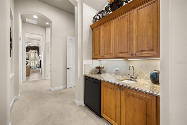 kitchen with dishwasher, light stone counters, brown cabinets, arched walkways, and a sink