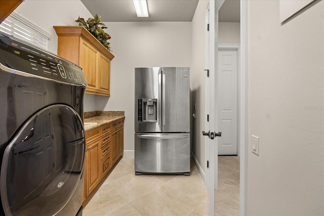 kitchen with baseboards, light stone countertops, stainless steel fridge with ice dispenser, brown cabinetry, and washer / clothes dryer