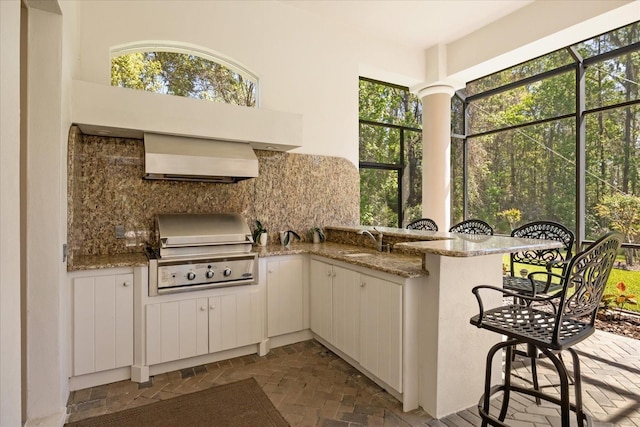 kitchen with a sink, backsplash, a peninsula, brick floor, and light stone countertops