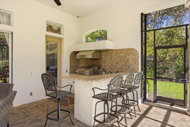 interior space featuring a breakfast bar area, wall chimney exhaust hood, brick floor, and a wealth of natural light