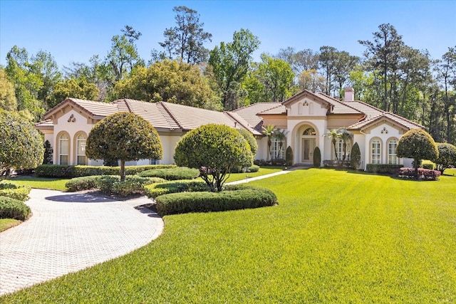 mediterranean / spanish home featuring stucco siding, a chimney, a front yard, and a tile roof