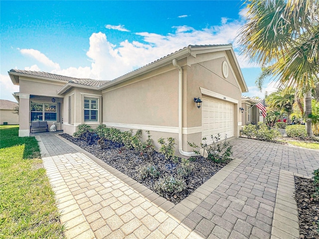 view of front of house with stucco siding, an attached garage, a tile roof, and driveway