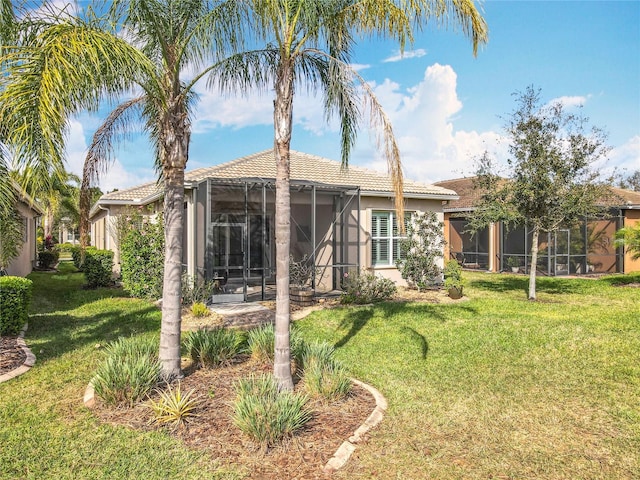 rear view of house featuring stucco siding, a sunroom, a lawn, and a tiled roof