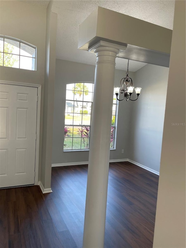 entryway with dark wood-style floors, baseboards, ornate columns, a textured ceiling, and a chandelier