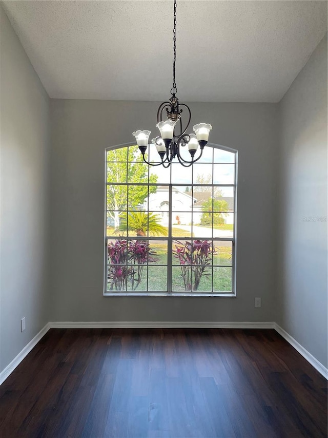 unfurnished dining area featuring a textured ceiling, baseboards, dark wood-style flooring, and a chandelier