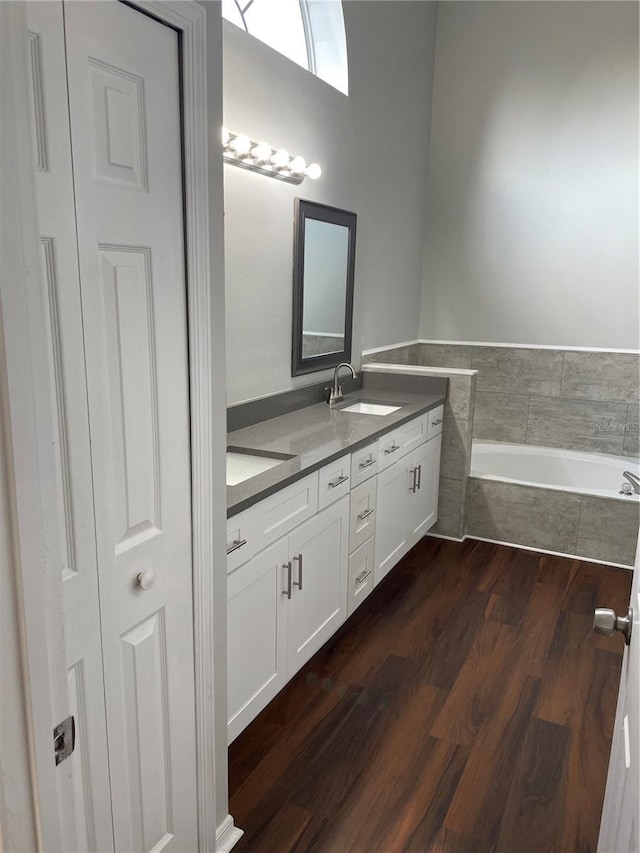 bathroom featuring a sink, wood finished floors, double vanity, and a bath