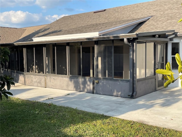 rear view of property with a sunroom, roof with shingles, and stucco siding