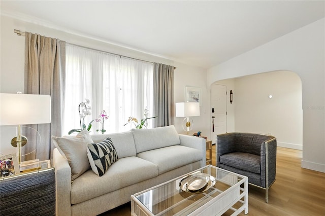 living area with vaulted ceiling, baseboards, arched walkways, and light wood finished floors