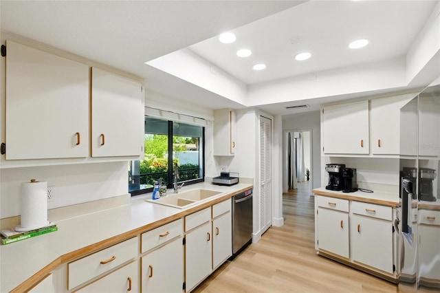 kitchen with a sink, white cabinetry, light wood-style floors, light countertops, and dishwasher