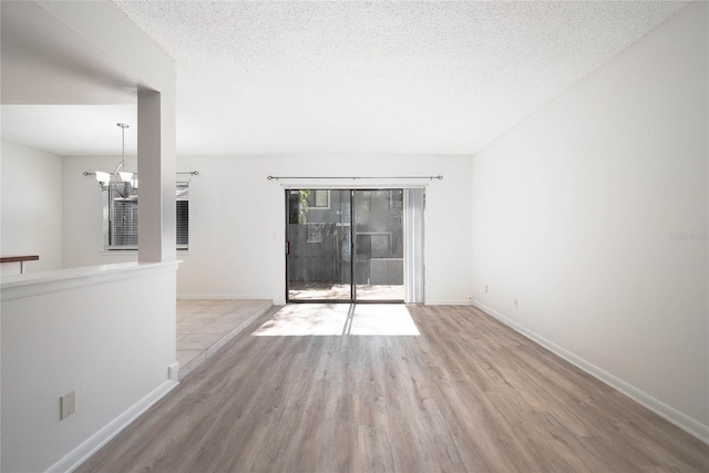 spare room with wood finished floors, baseboards, a chandelier, and a textured ceiling